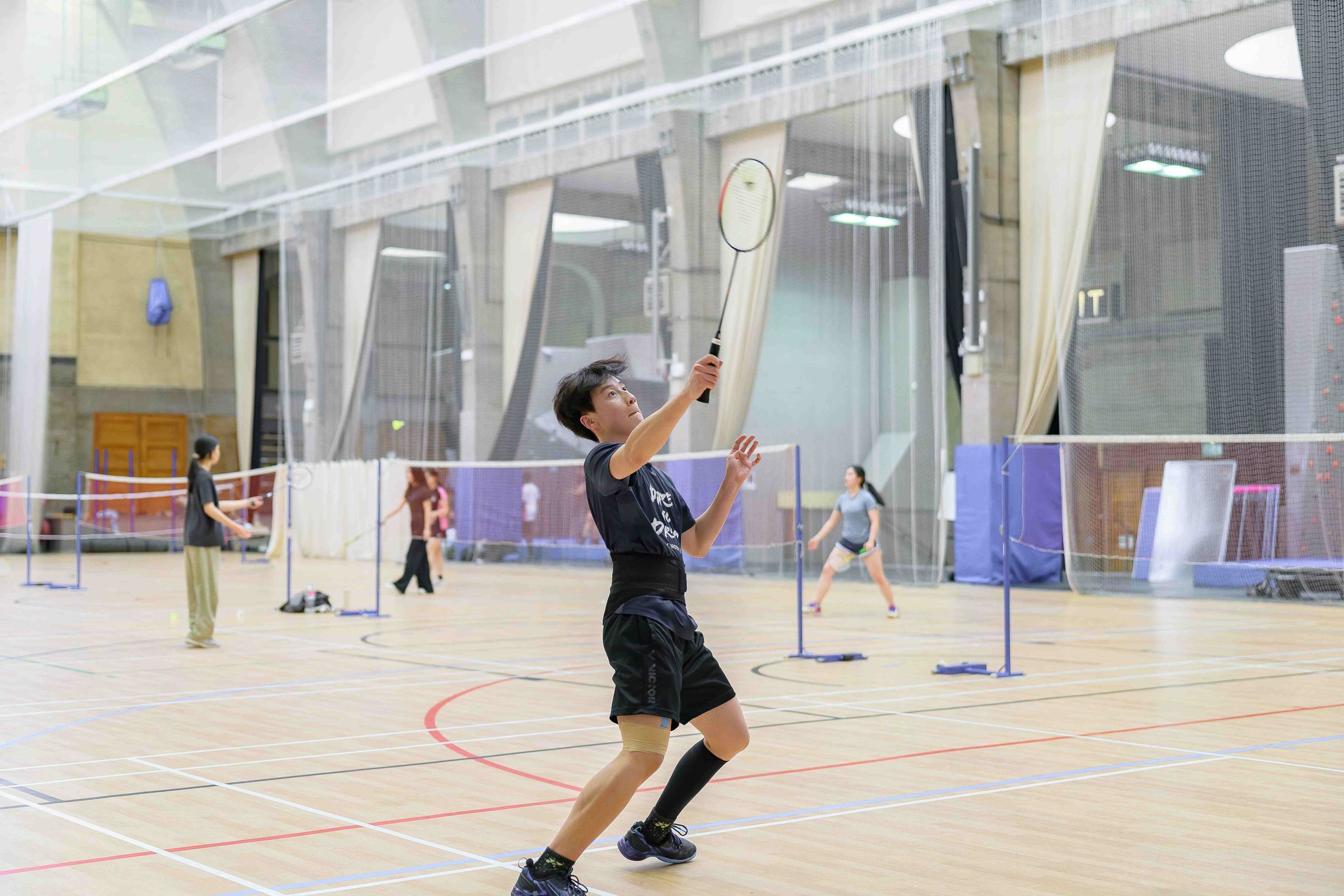 A boy playing badminton in the sports centre, just about to hit the shuttlecock in a volley