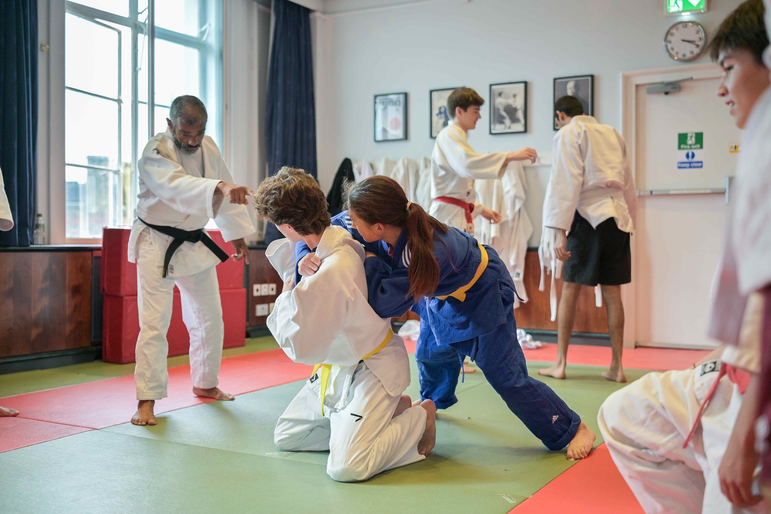 Two boys competing in Judo, on the floor, with the instructor giving advice