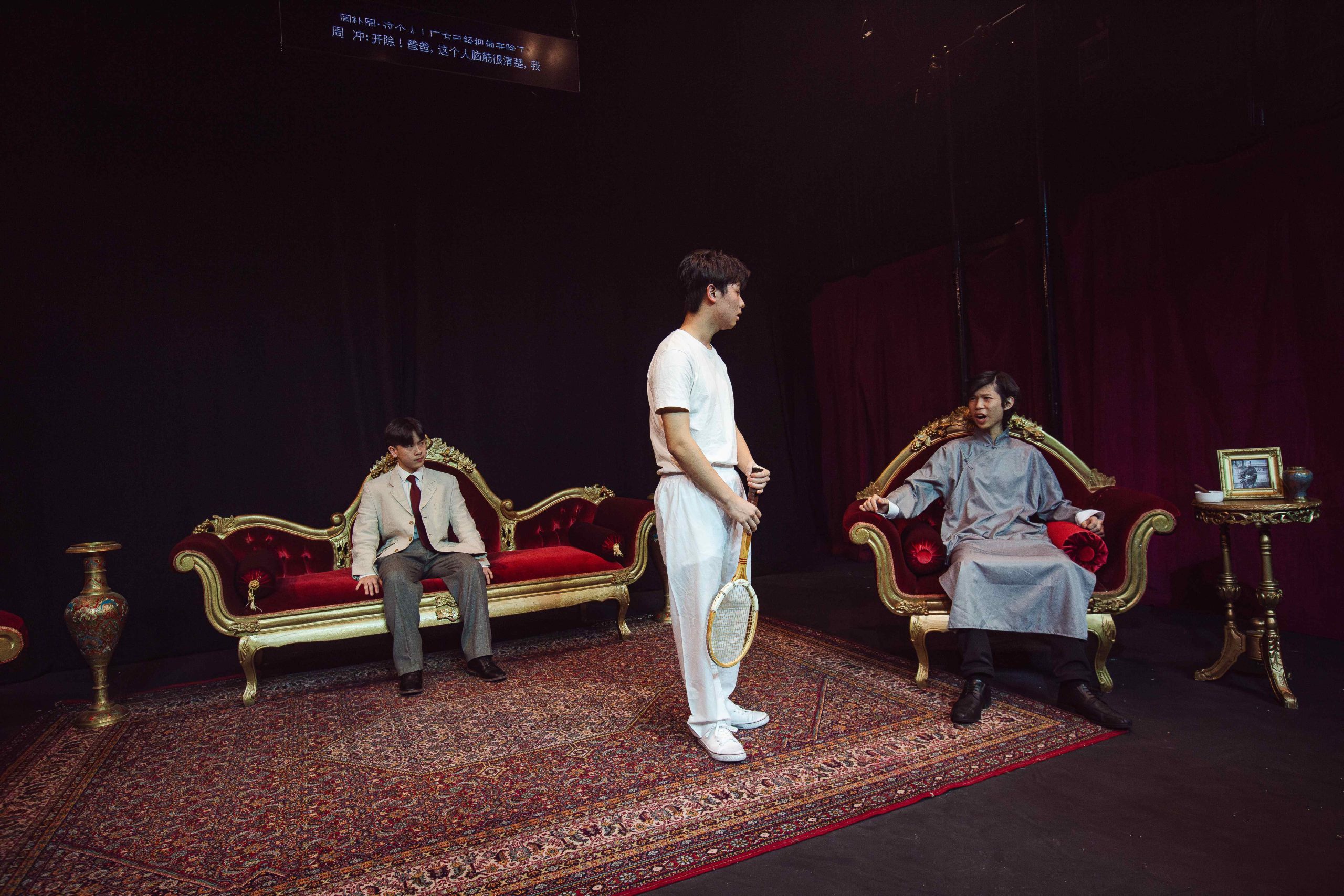 Three boys on stage, one stood up and two sat down