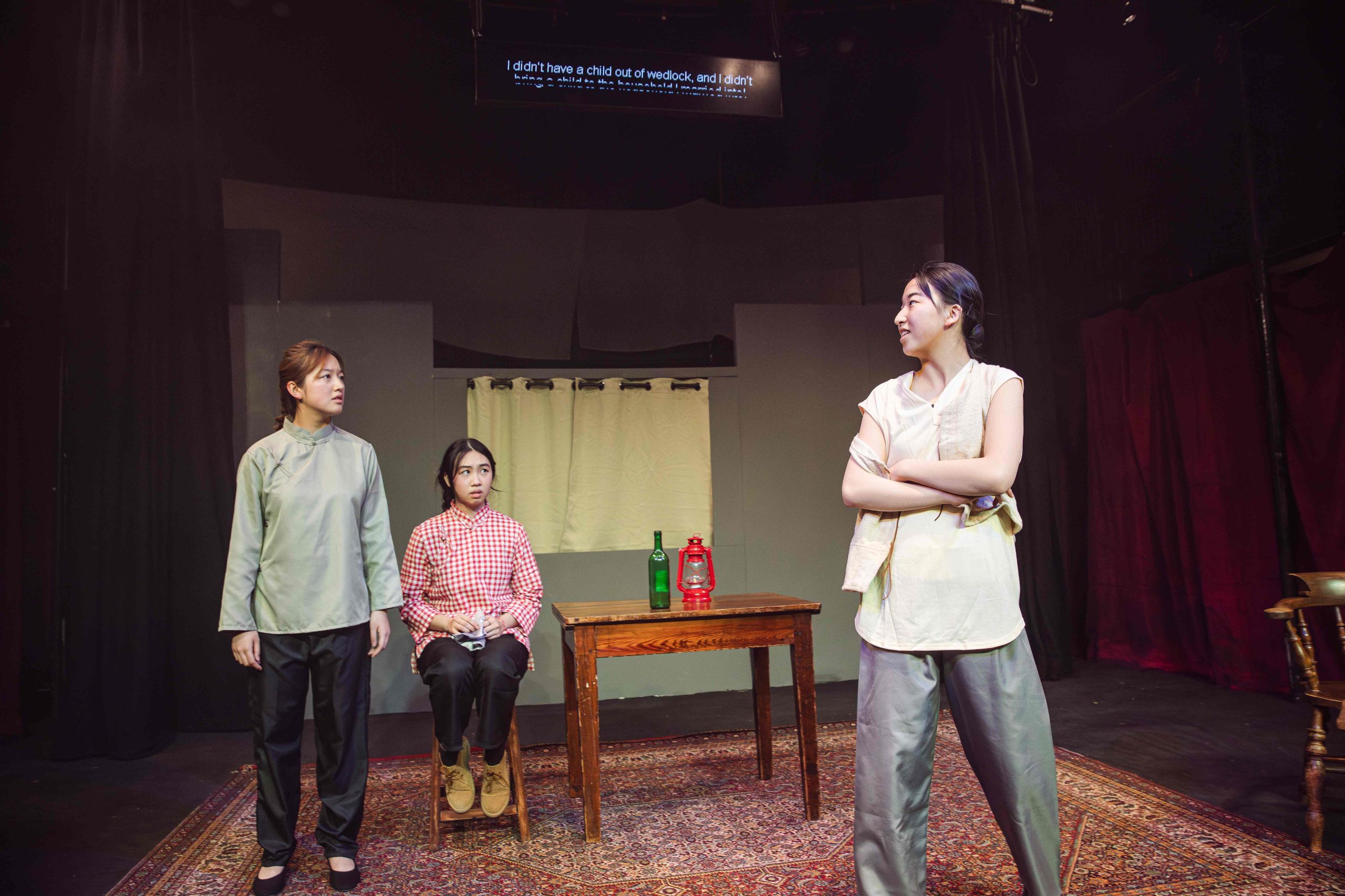 Three girls on stage acting, two stood up and one sat down