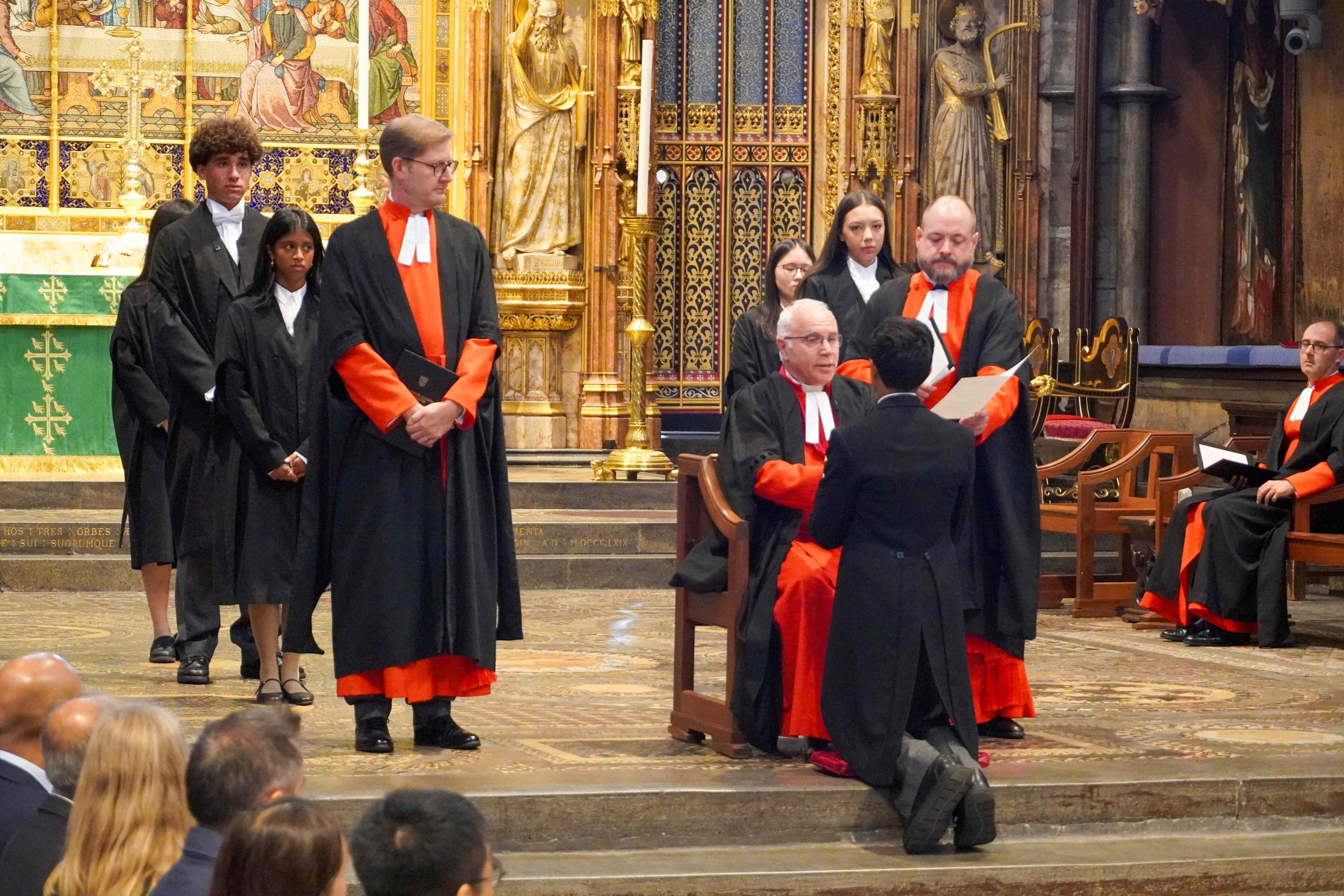 The Induction of the King's Scholars in Westminster Abbey in September 2025. The Dean is in the foreground, with the Head Master and the Master of the King's Scholars; a boy is on his knees in front of the Dean being inducted. The rest of the inducted Scholars are behind in lines.