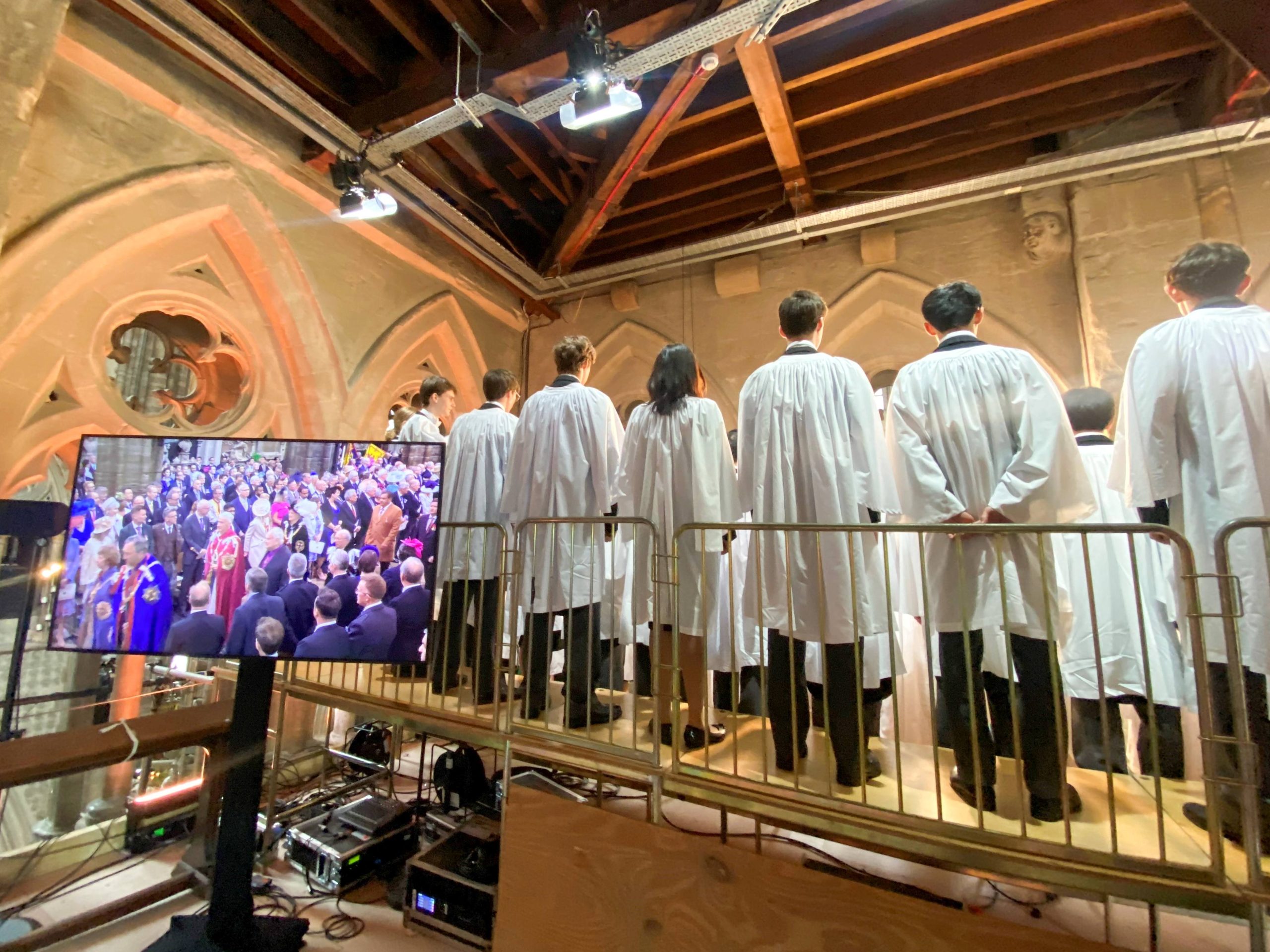 Coronation Day 2023. The King's Scholars are lined up ready to be the first to proclaim Vivat at the new Monarch. The photo is taken from behind and there is a screen to the left showing the crowds in Abbey with the King in the centre.