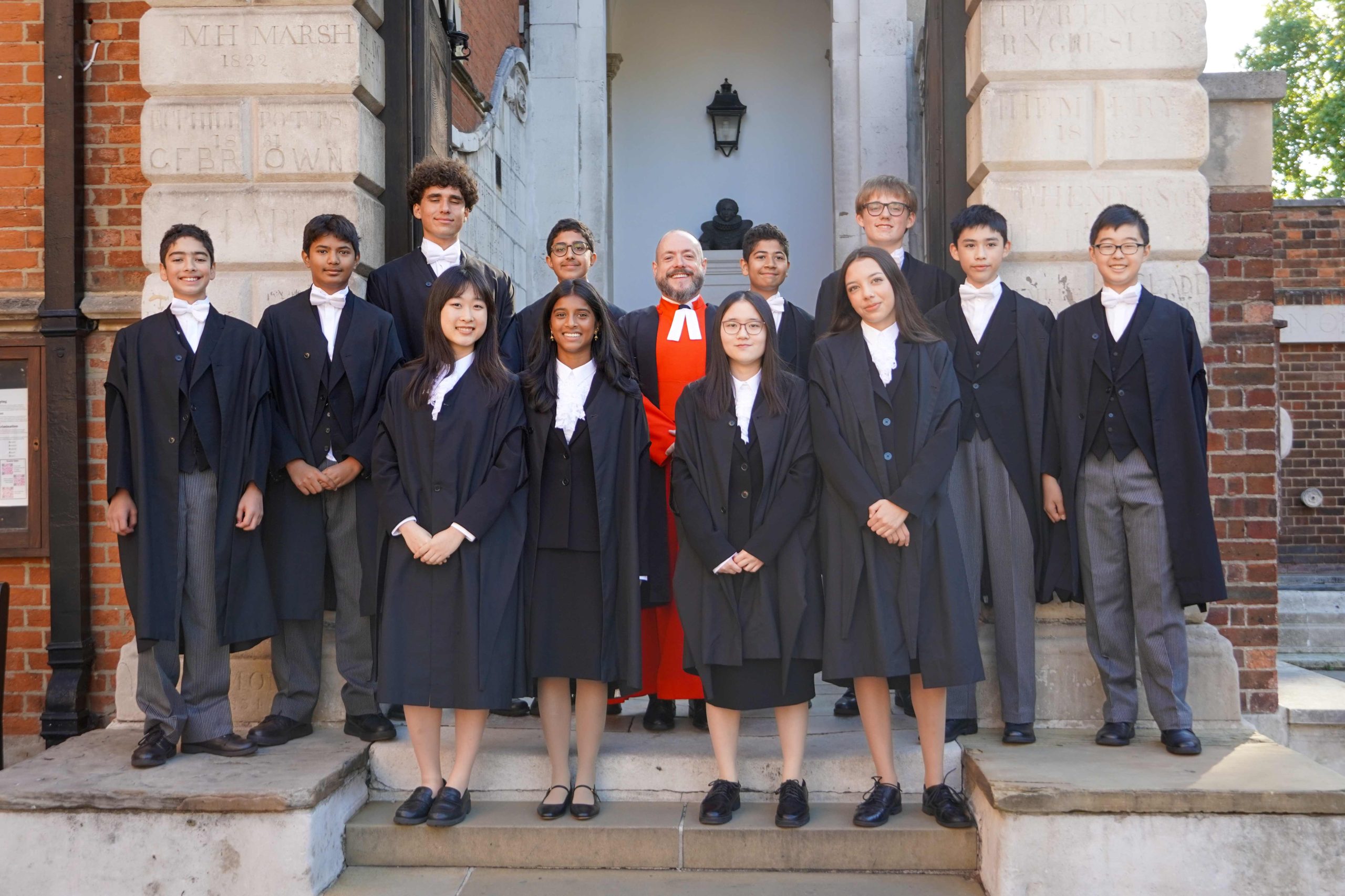 2025's King's scholars standing by the arch to School in Little Dean's Yard with the Master of the King's Scholars at the centre. On their induction day.