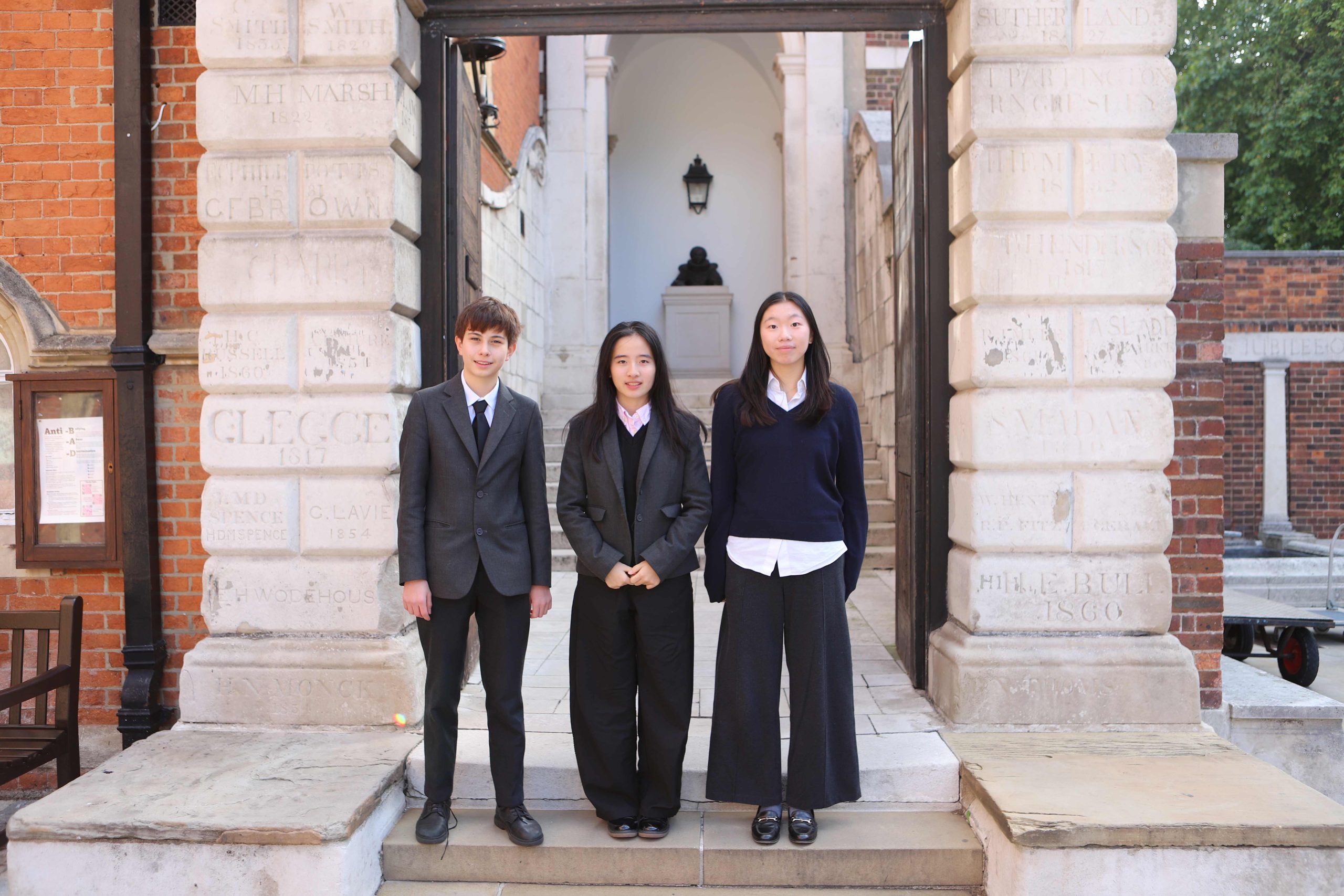 Three 2025 Academic Exhibitioners standing by the arch to School in Little Dean's Yard.