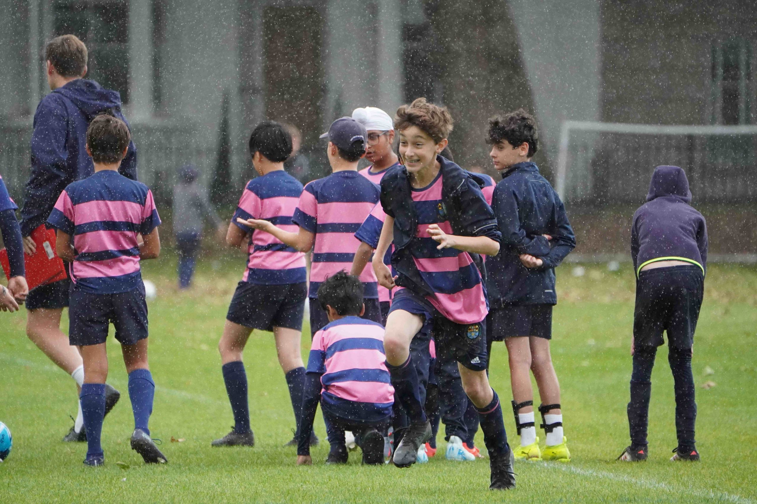 Westminster Under School boys standing on the football pitch in sports clothing, with one boy running and smiling at the centre.