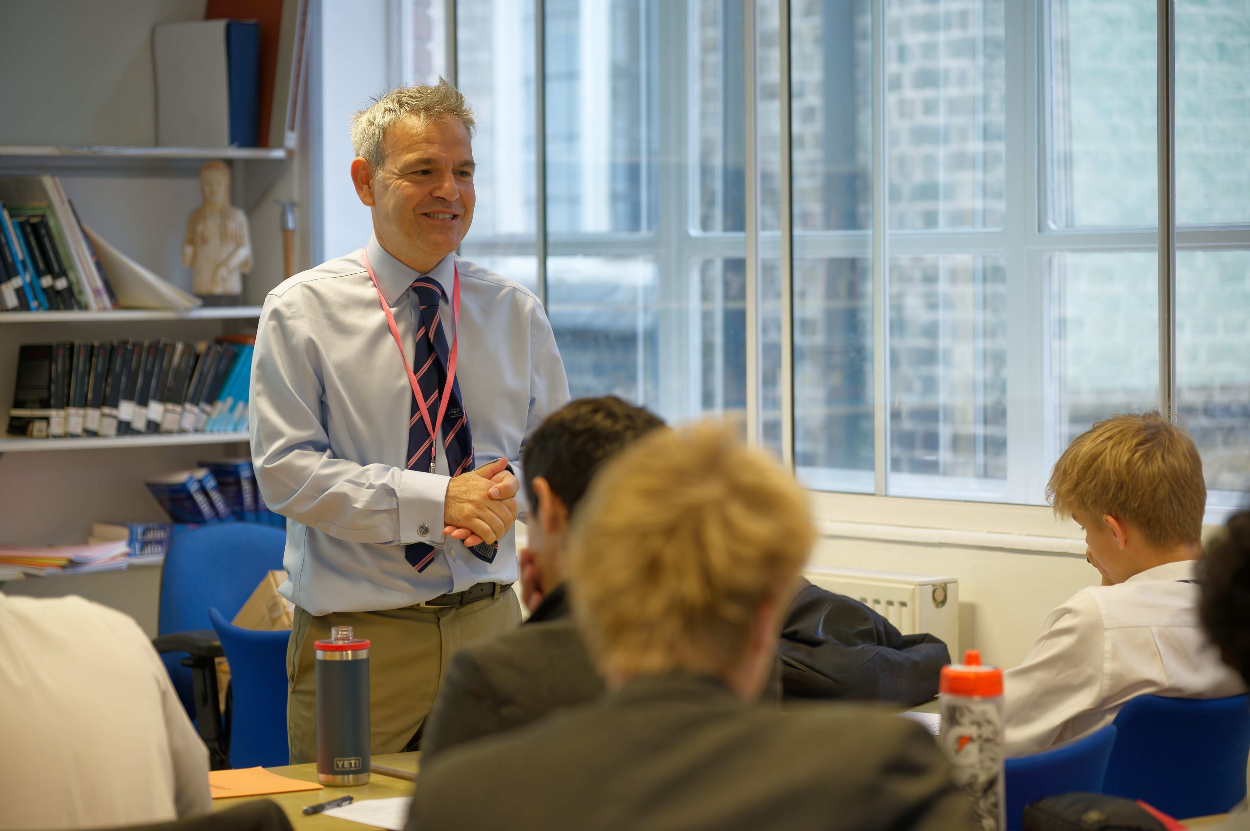 A teacher, hands together, smiling at his class