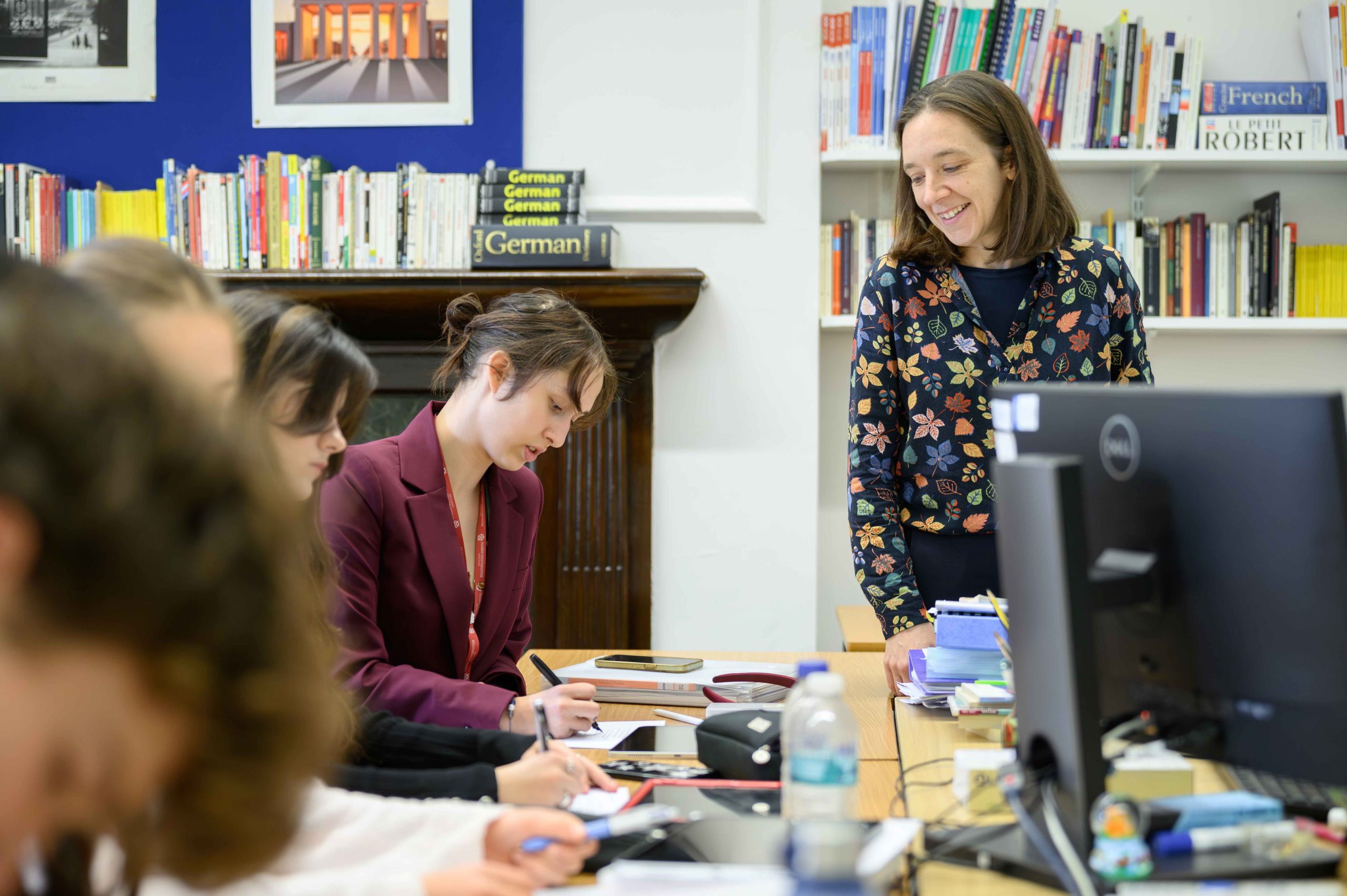 A German teacher smiling, with pupils writing notes at their desks