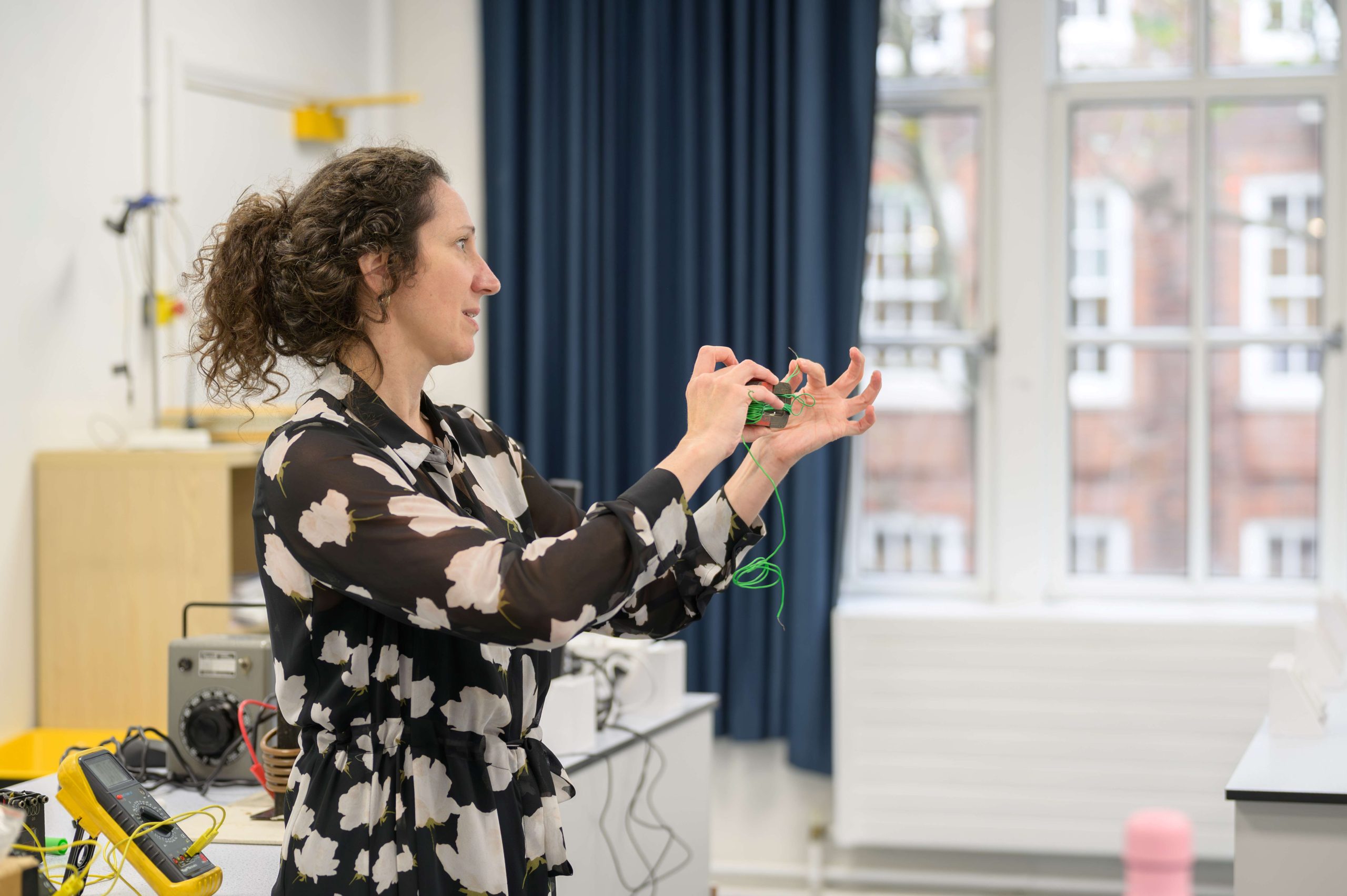 A female Physics teacher showing the class how to conduct an experiment with wires in the lab