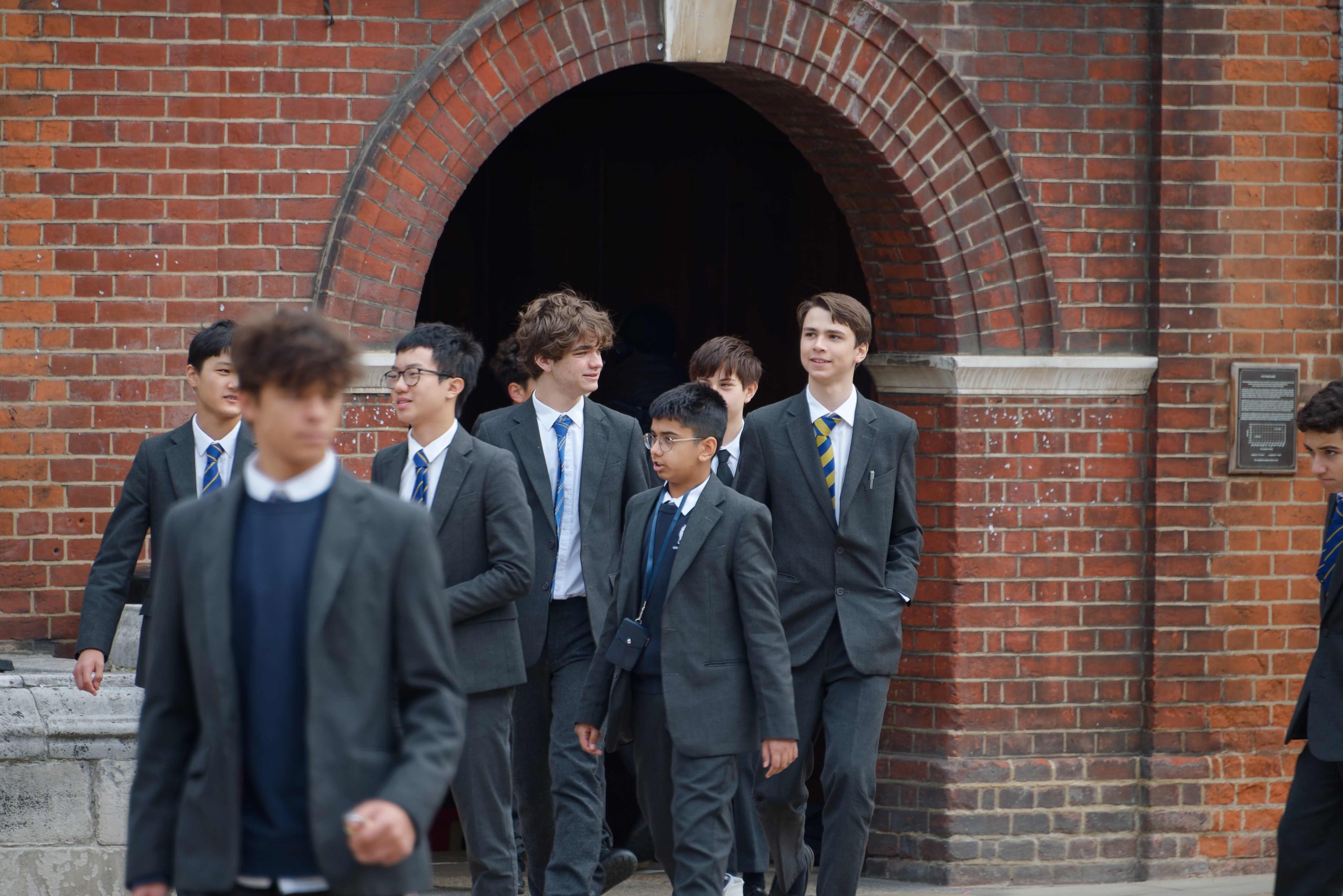 A group of boys of different ages walking out of a school building into Little Dean's Yard