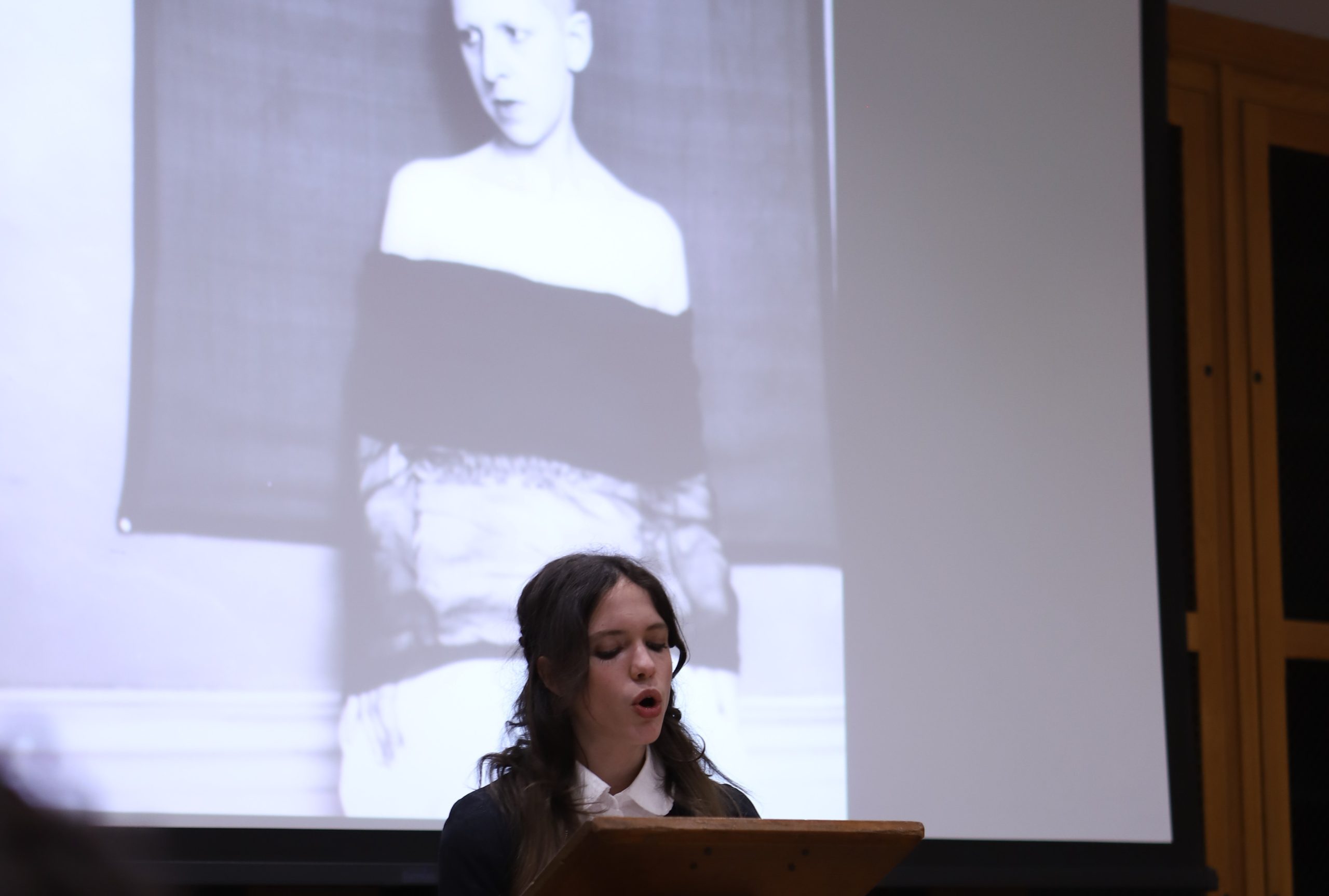 Pupil speaking on Claude Cahun in front of a screen with image of Cahun's self-portrait, standing in front of the lectern.