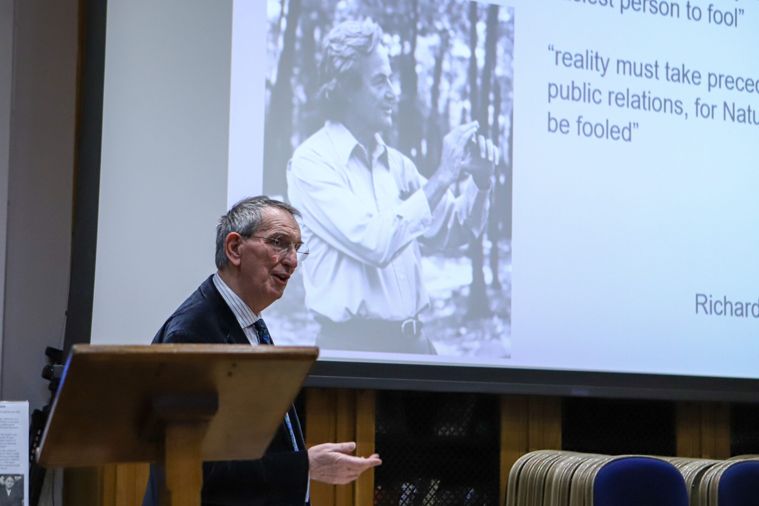 Professor Lockwood speaking with an image of Richard P Feynman on the screen behind him