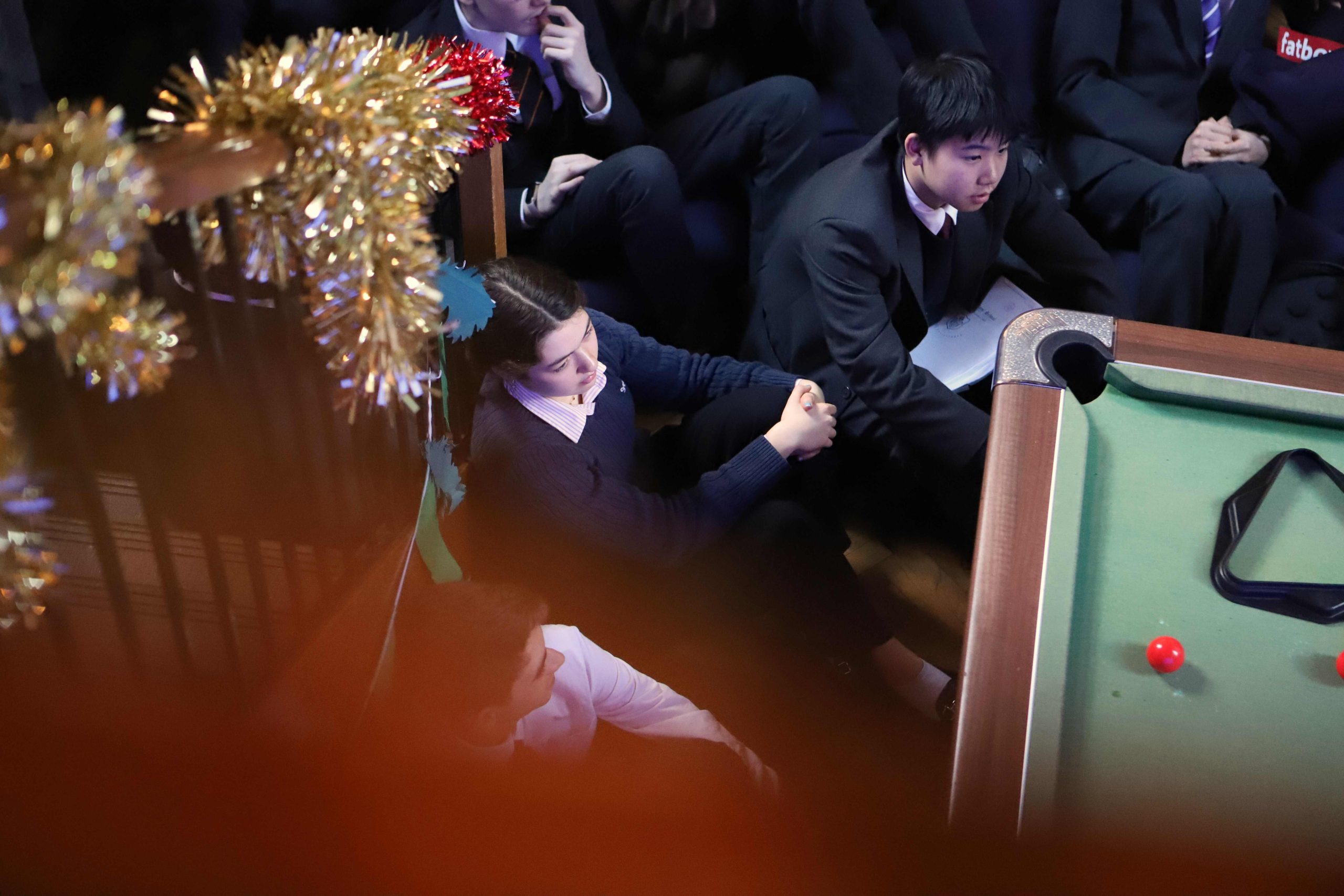 Pupils sat down, a girl at the centre, watching the talk. Birdseye view, taken from the top of the stairs.