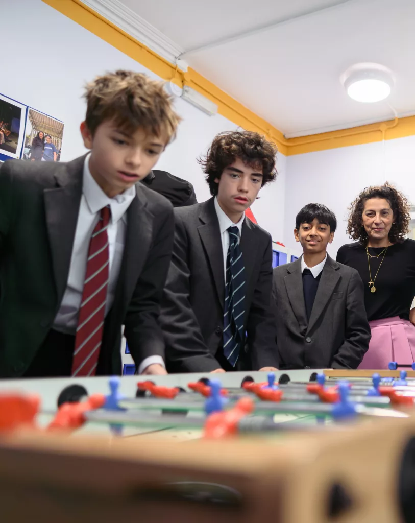 Three boys in uniform playing table football with their housemaster looking at the game