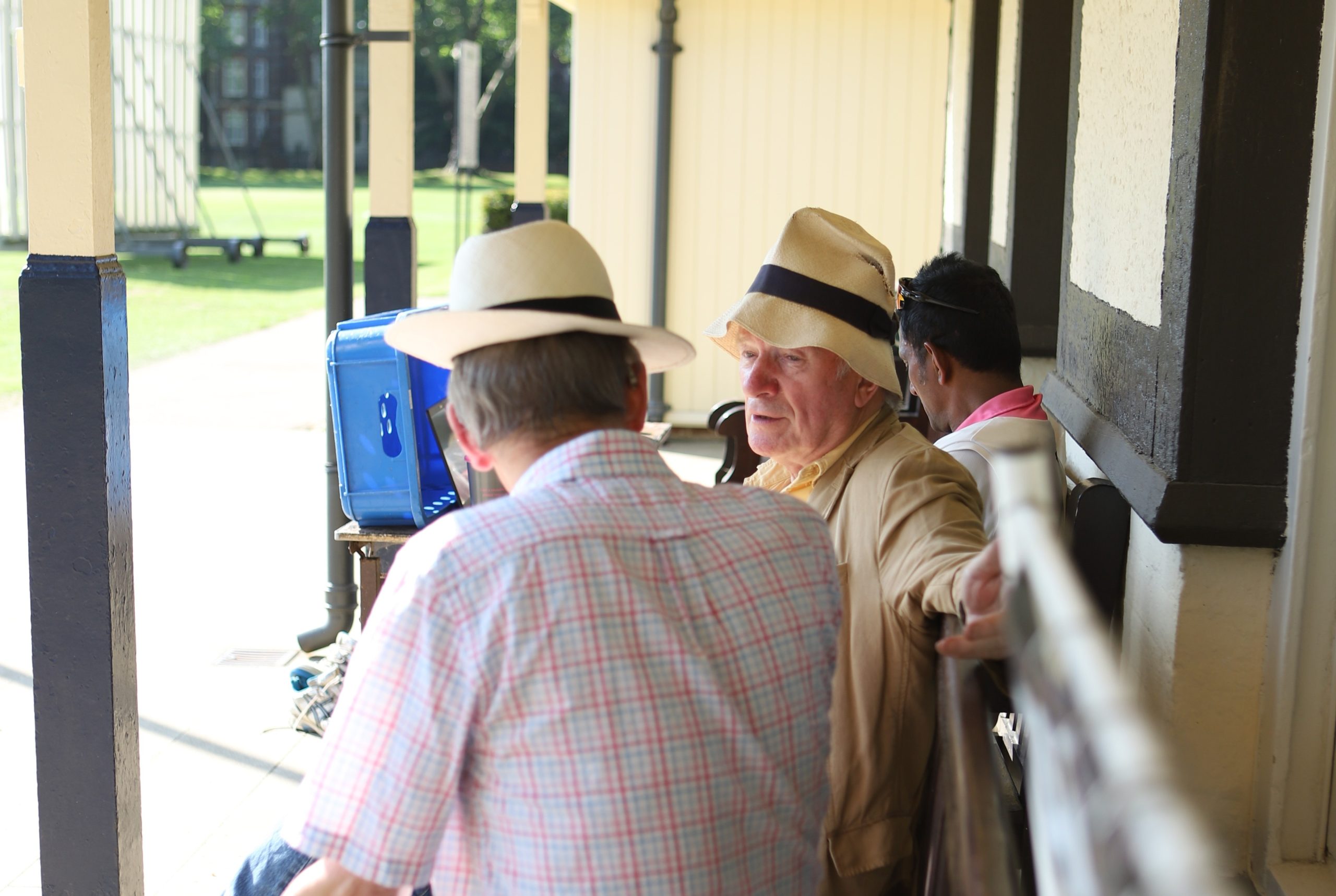 Two men in straw hats sat chatting on a bench under the pavilion canape