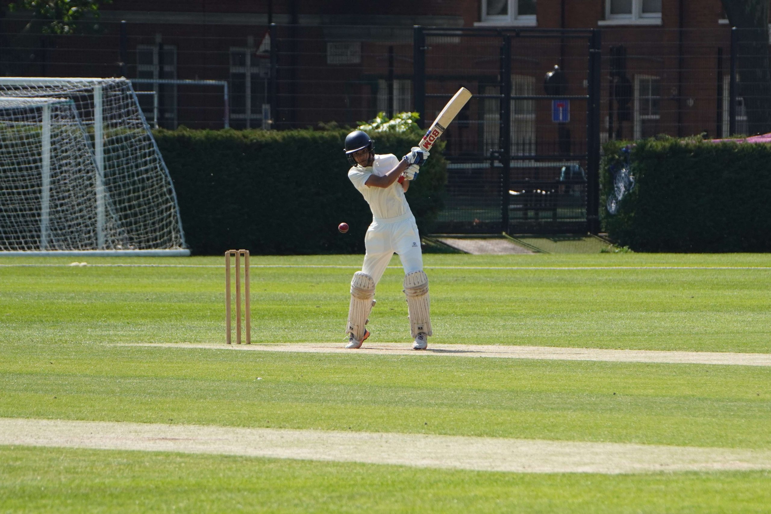 A Westminster pupil has just batted with his bat in the air, he is i whites and a helmet and the wicket is behind him to the left of the image