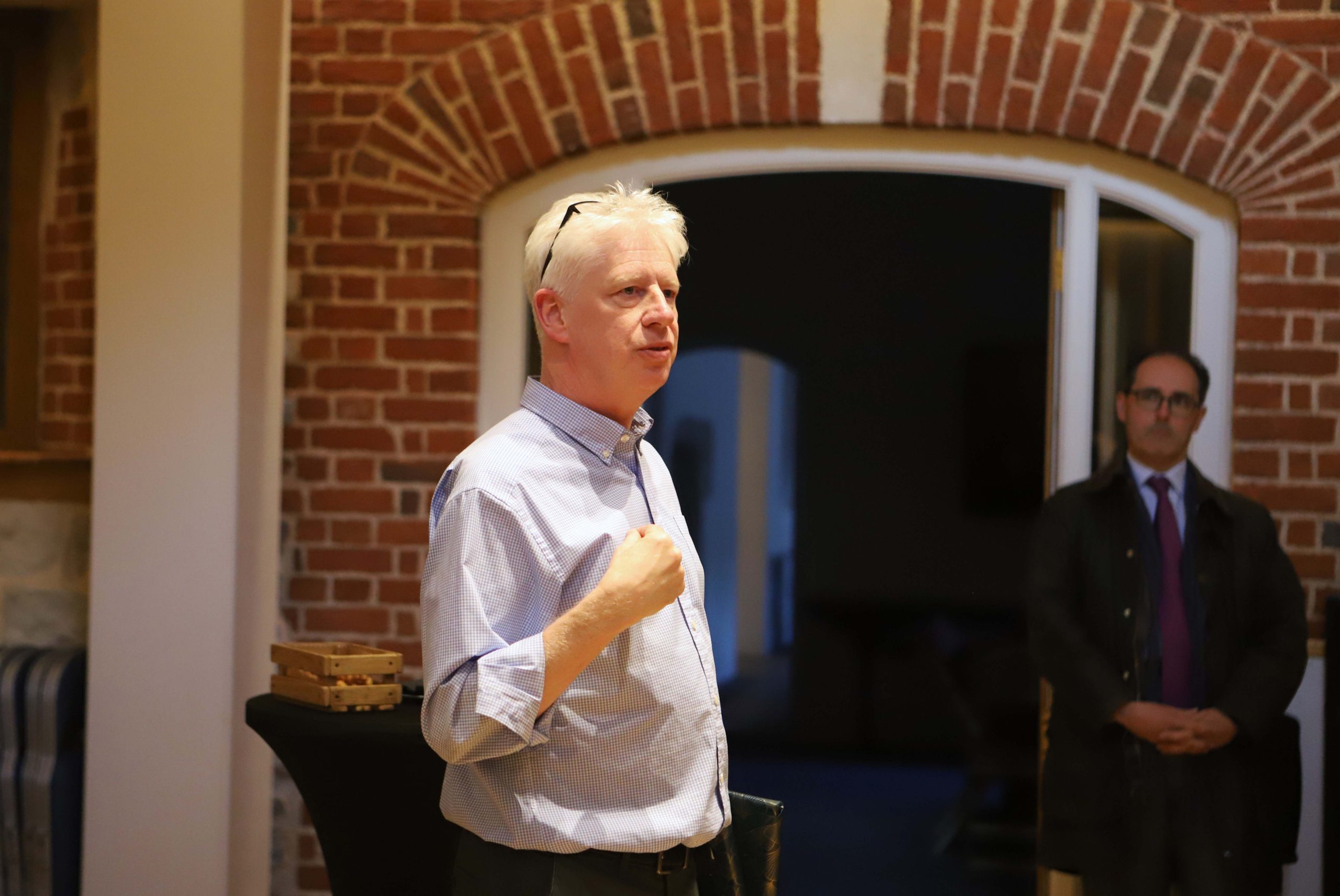 A male teacher speaking in a school venue with a red brick archway to another room behind him
