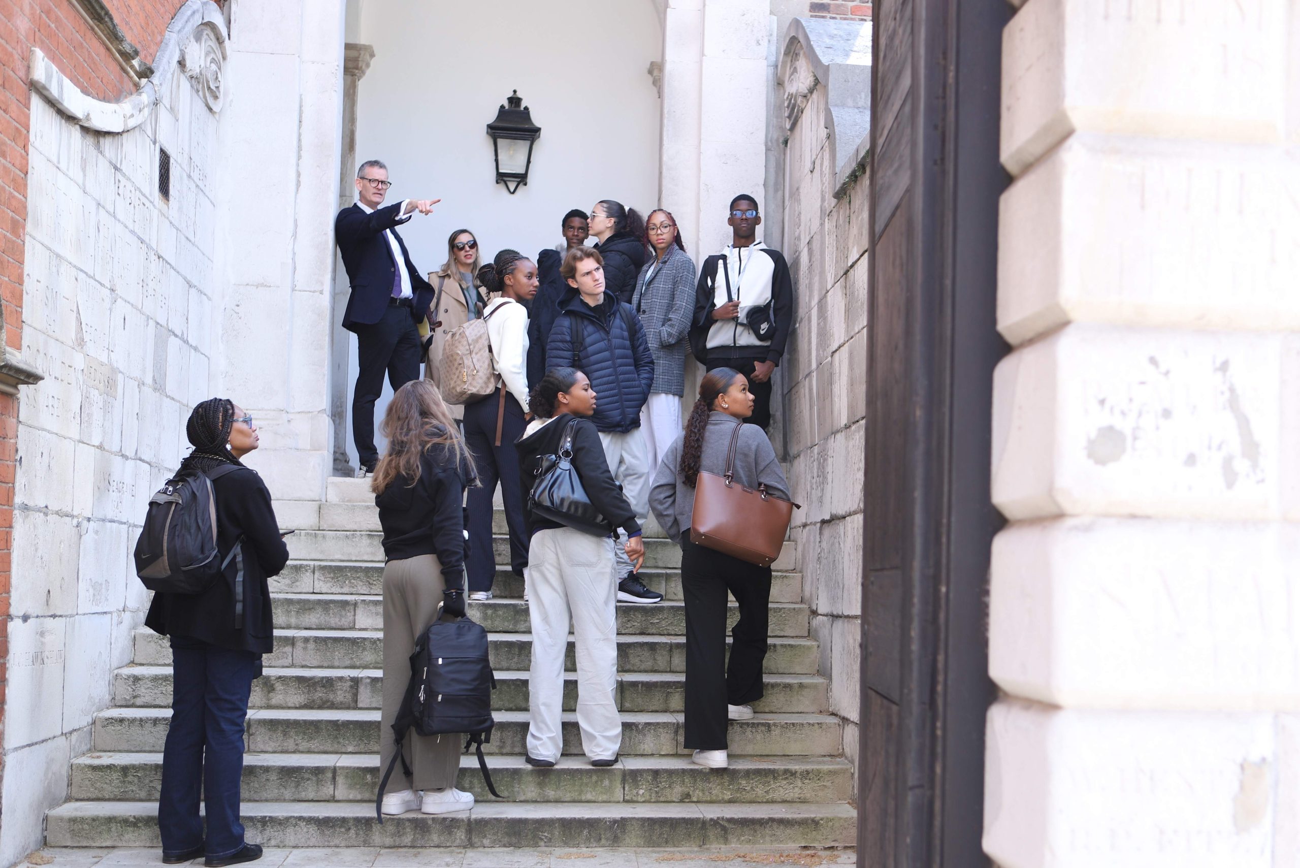 Group of Martinique pupils on the stone steps up to Westminster's school hall looking at something that their male tour guide has pointed out